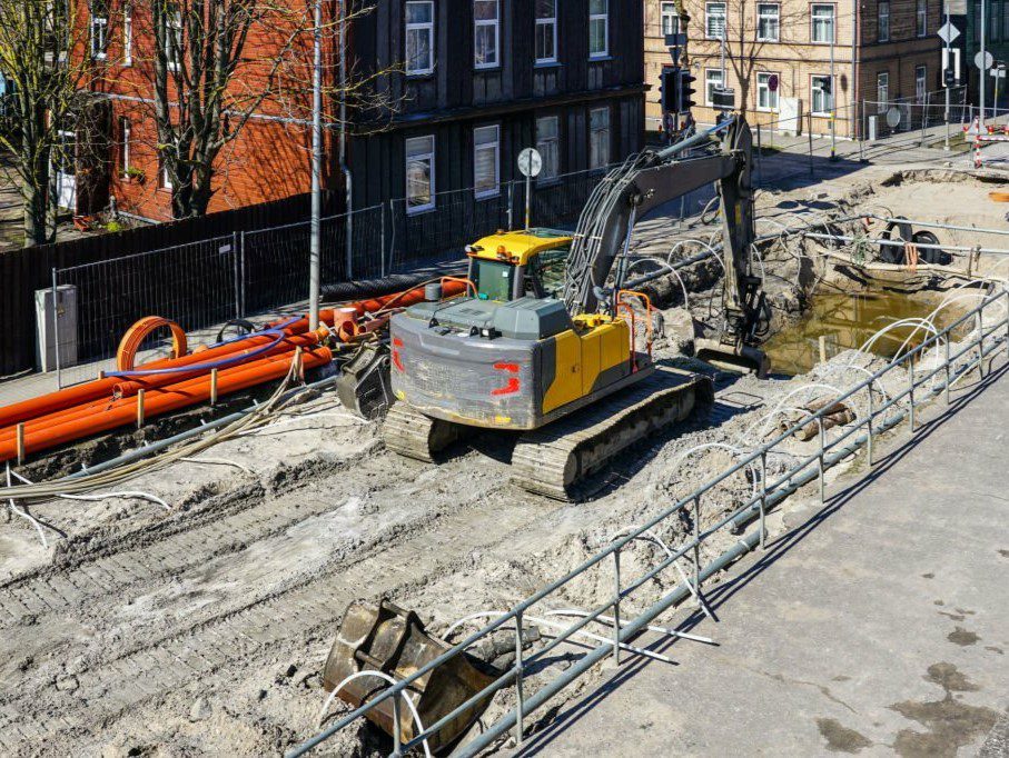 Underground pipeline replacement site with dewatering system on city street, excavator digs deep trench, top view